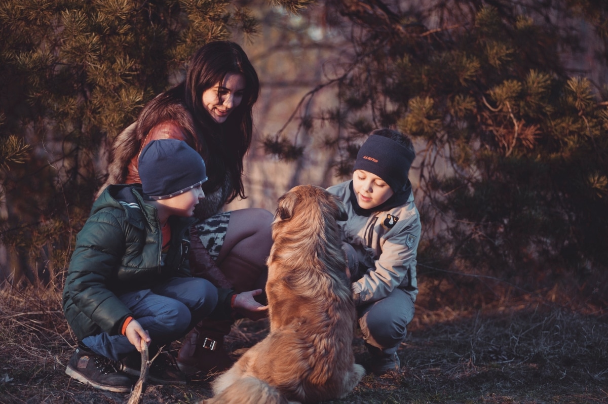 two boys with their mum and the family dog happily crouching in a wooded area